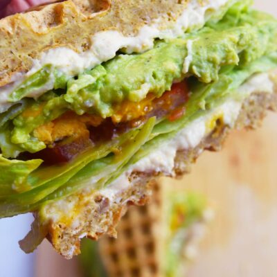 A hand holds half a Breakfast Mediterranean Sandwich over a wood cutting board.