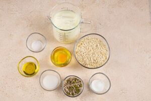 Oat bread ingredients gathered on an off-white surface in idividual glass bowls.