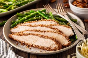 Sliced chicken breast on a plate with green beans.