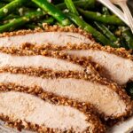 Sliced pecan crusted chicken on a plate with garlic green beans.