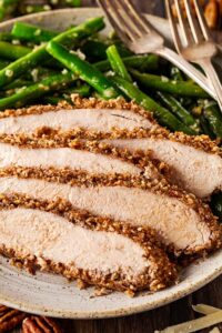 Sliced pecan crusted chicken on a plate with garlic green beans.