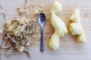 Two pieces of peeled ginger on a cutting board with a spoon and the peels in a pile. All on a cutting board. Overhead focus.
