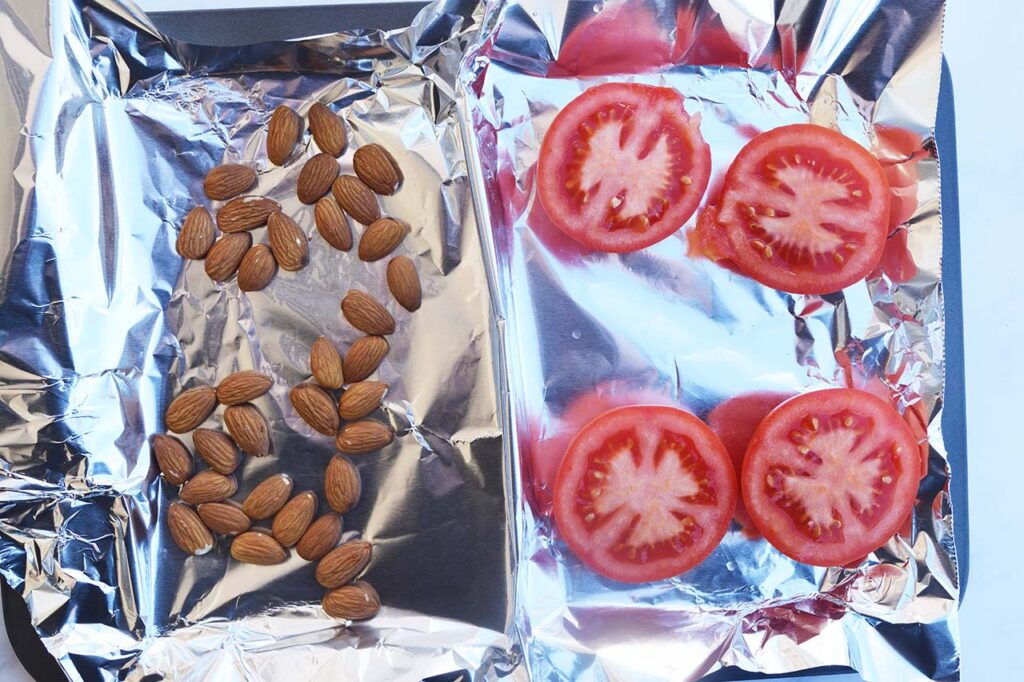 Raw almonds and halved tomatoes on a roasting pan.