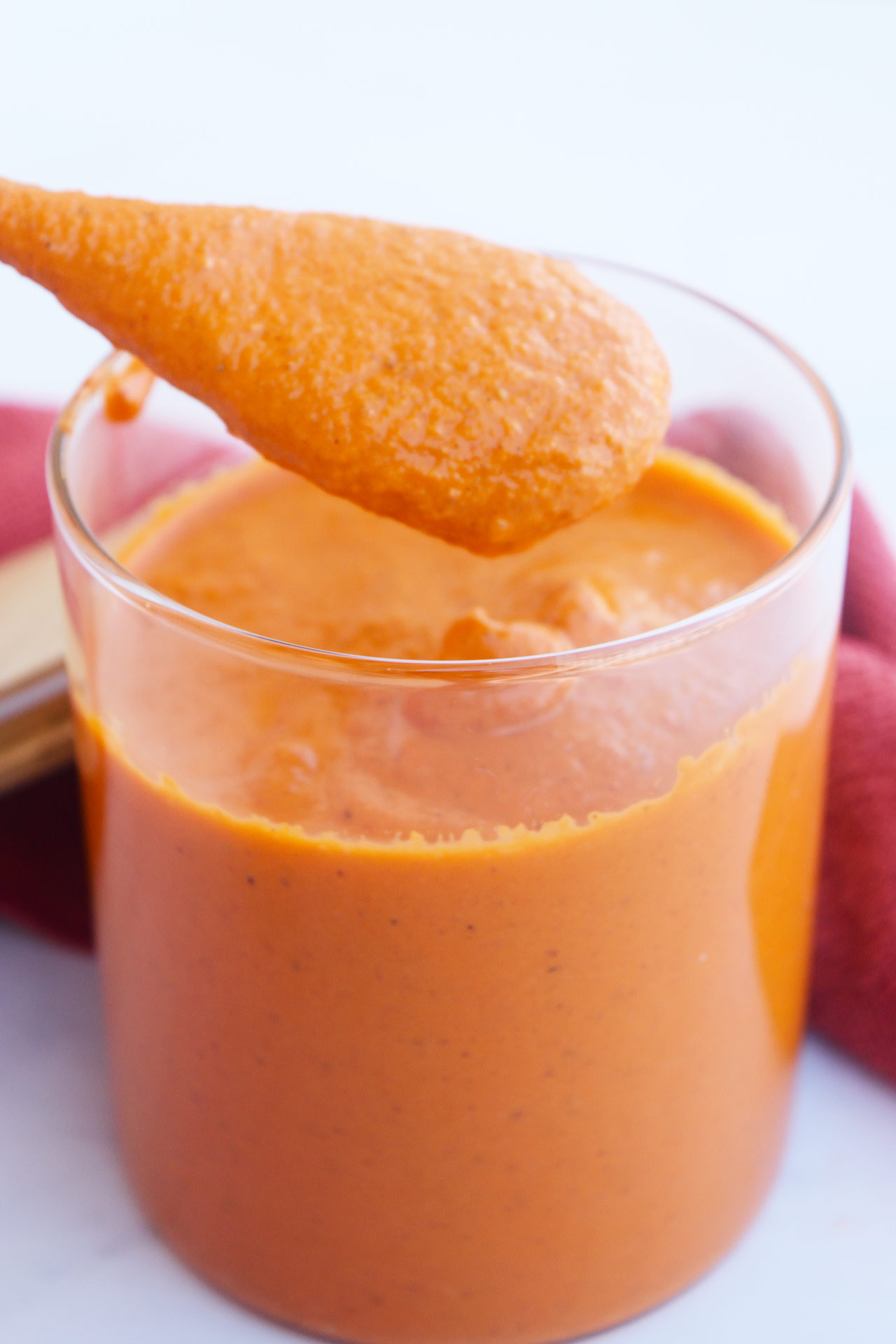 Front view of a wood spoon lifiting Romesco Sauce out of a glass jar.