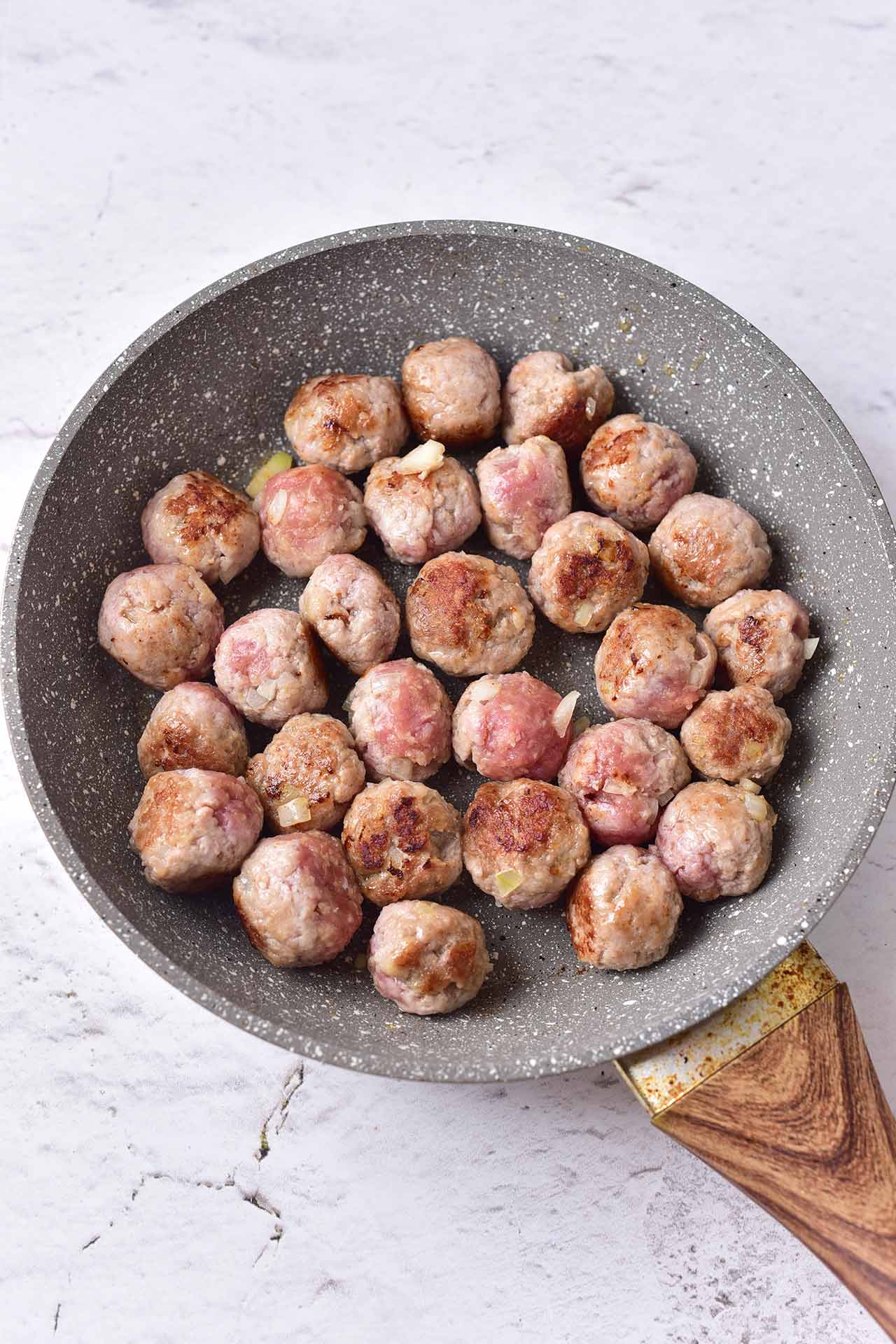 Meatballs browning in a skillet.