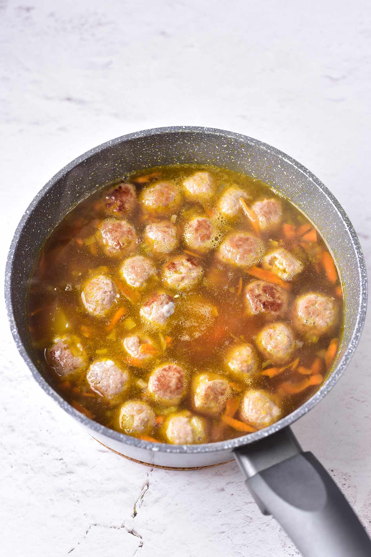 Browned meatballs added to a pot of broth and vegetables.
