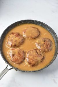 Turkey Salisbury Steak patties sitting in gravy in a skillet.