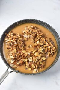 Mushrooms spooned over Turkey Salisbury Steaks sitting in gravy in a skillet.