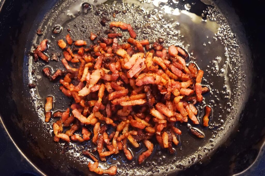 Bacon bits cooking in a skillet.