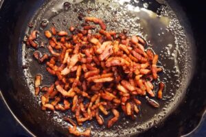 Bacon bits cooking in a skillet.