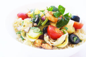 Mediterranean Shrimp Salad served over cooked quinoa in a white bowl. White background.