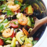 Partial view of a mixing bowl filled with Mediterranean Shrimp Salad and a wooden spoon.