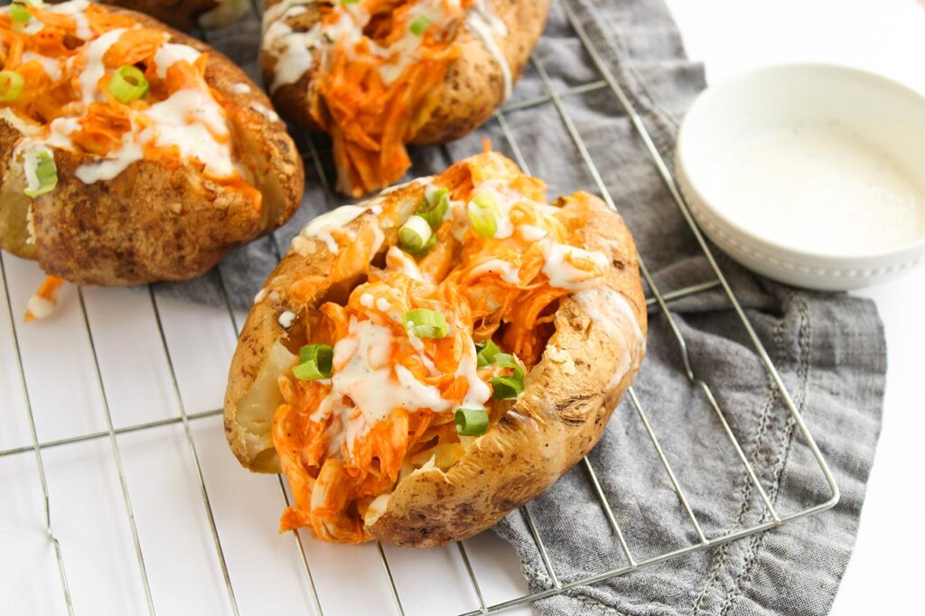 Horizontal orientation. Three Buffalo Chicken Stuffed Baked Potatoes sitting on a cooling rack.