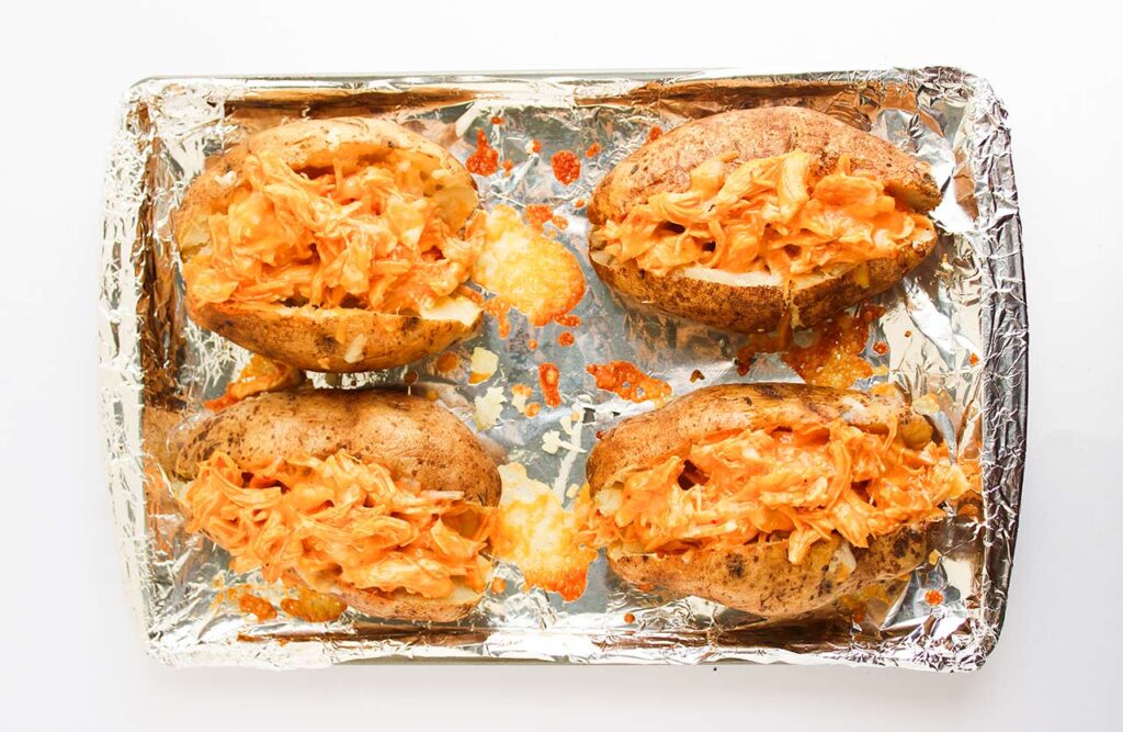 Four stuffed baked potatoes on a baking pan, cooling after baking a second time to melt the cheese added to the top.