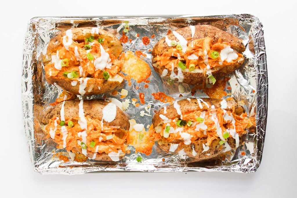 Four Buffalo Chicken Stuffed Baked Potatoes drizzled with ranch dressing. Overhead focus.