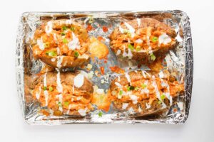 Four Buffalo Chicken Stuffed Baked Potatoes drizzled with ranch dressing. Overhead focus.