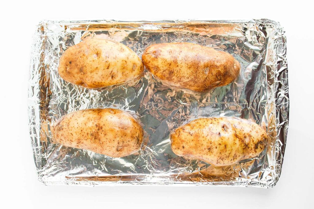 Oiled russet potatoes on a foil-lined baking pan. Overhead focus.