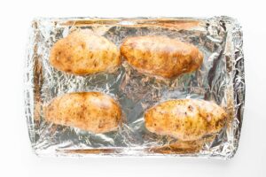 Oiled russet potatoes on a foil-lined baking pan. Overhead focus.