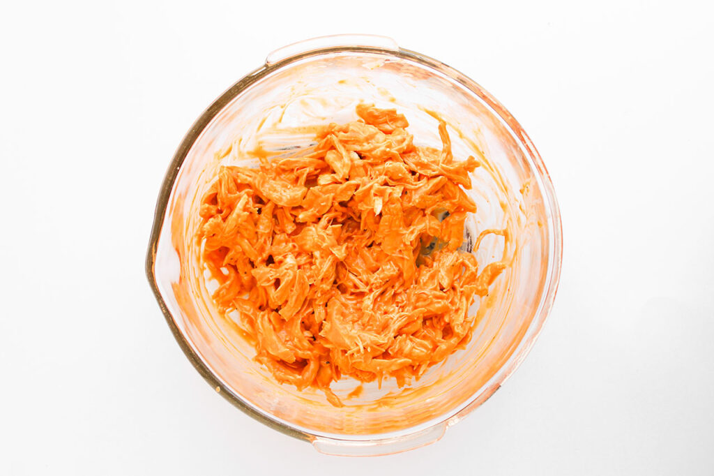 Chicken mixed with buffalo sauce in a mixing bowl. Overhead focus.