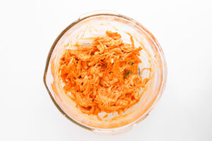 Chicken mixed with buffalo sauce in a mixing bowl. Overhead focus.