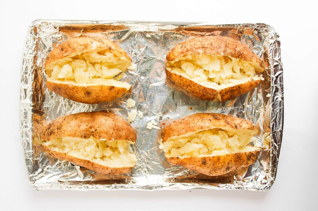 Four russet potatoes cut open lengthwise down the middle, sitting on a baking pan. Overhead focus.