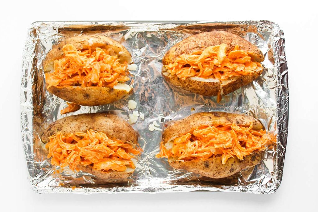 Four russet potatoes, cut open, stuffed with buffalo chicken. Overhead focus.