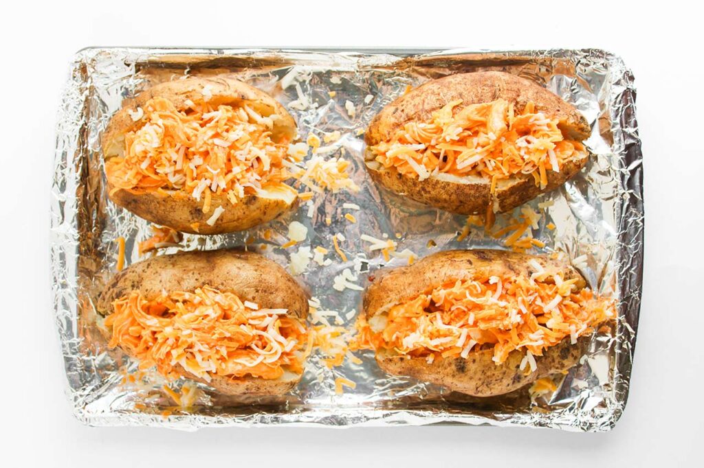 Four stuffed potatoes topped with grated cheese. Overhead focus.