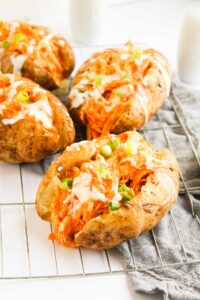 Front view of four Buffalo Chicken Stuffed Baked Potatoes on a wire, metal cooling rack.