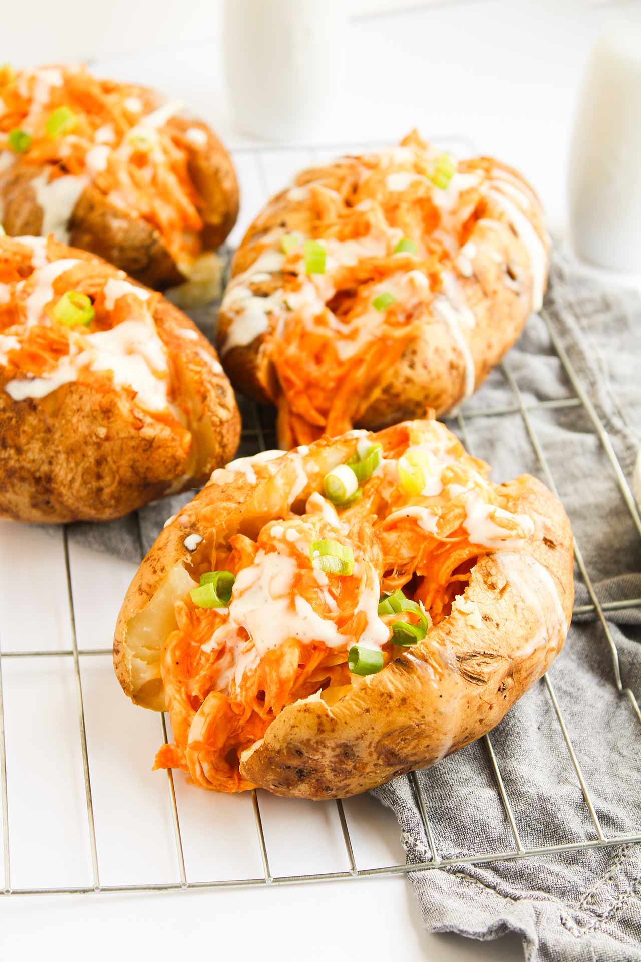 Front view of four Buffalo Chicken Stuffed Baked Potatoes on a wire, metal cooling rack.