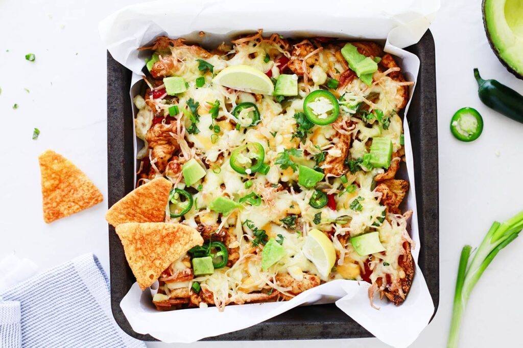A pan of Chicken Fajita Nachos garnished with avocado and jalapeno slices.