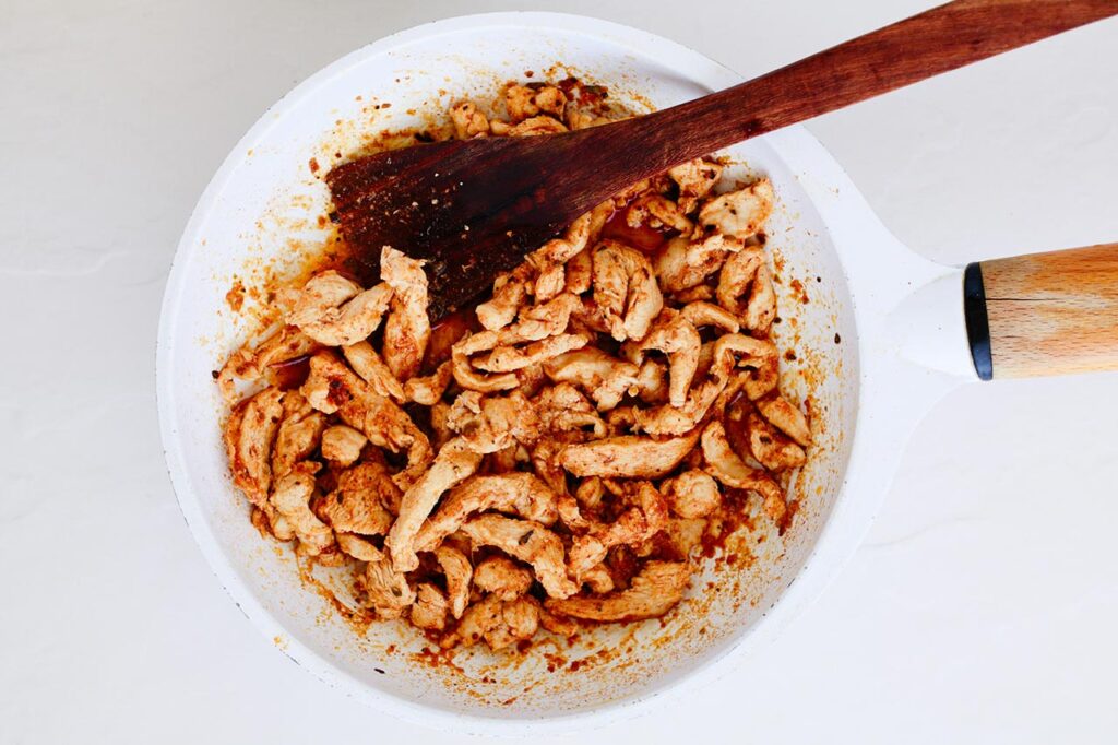 Mixed chicken and spices in a skillet.