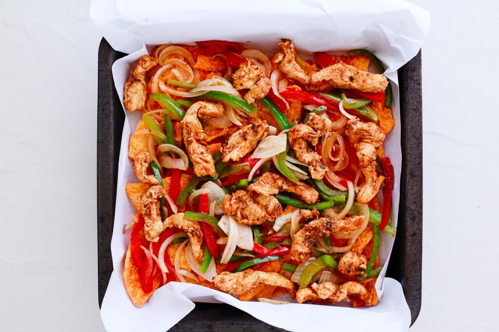 Chicken and veggies over corn chips on a parchment-lined sheet pan.