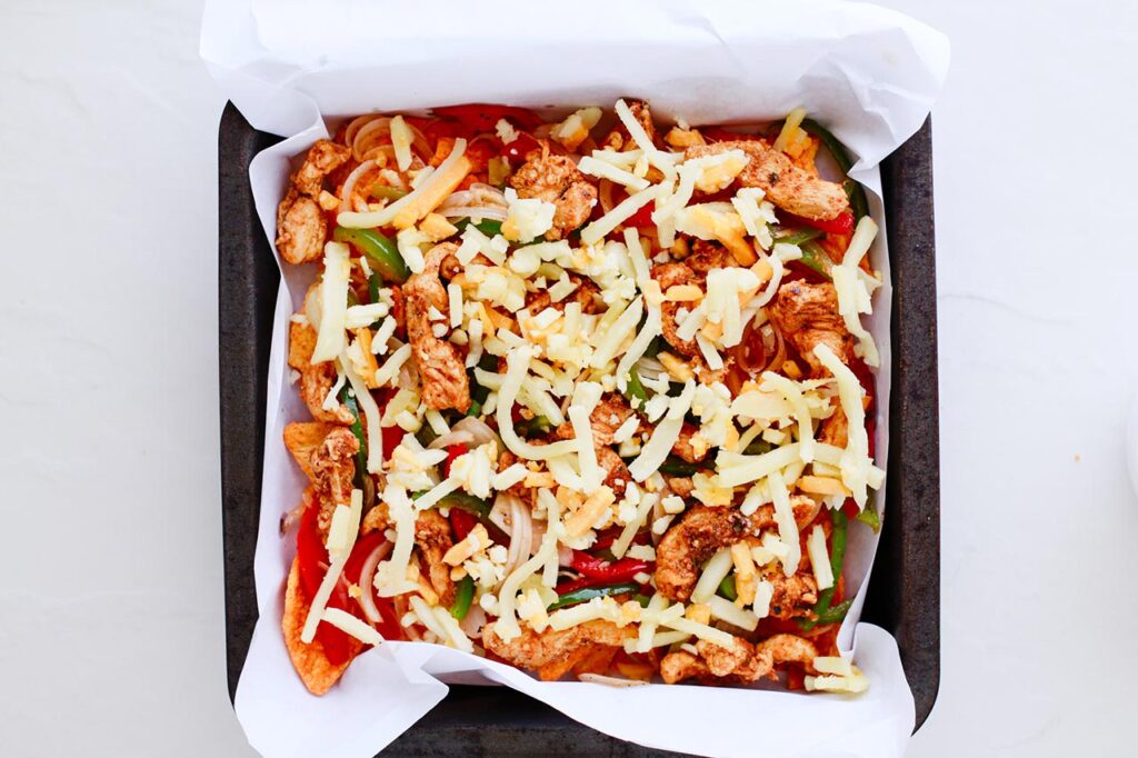 Cheese sprinkled over chicken veggies and chips on a sheet pan.