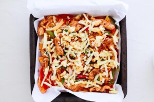 Cheese sprinkled over chicken veggies and chips on a sheet pan.