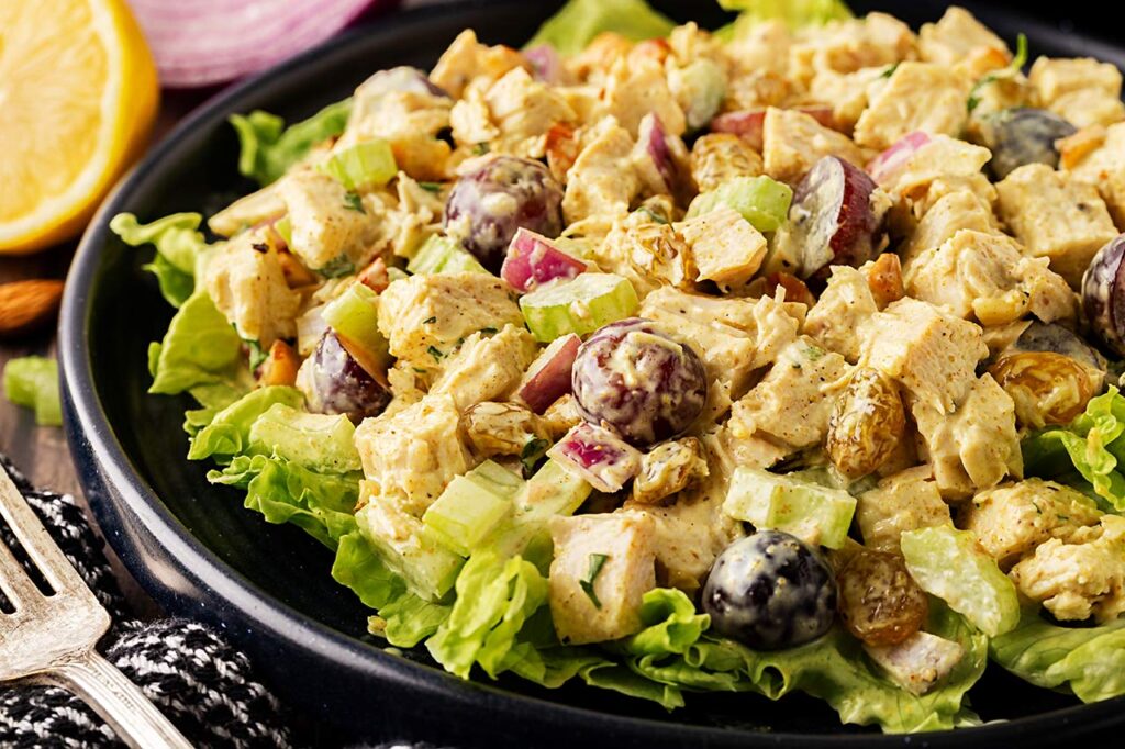 Front, partial view. Black plate holds curried chicken salad served over lettuce greens.