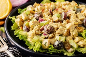 Front, partial view. Black plate holds curried chicken salad served over lettuce greens.