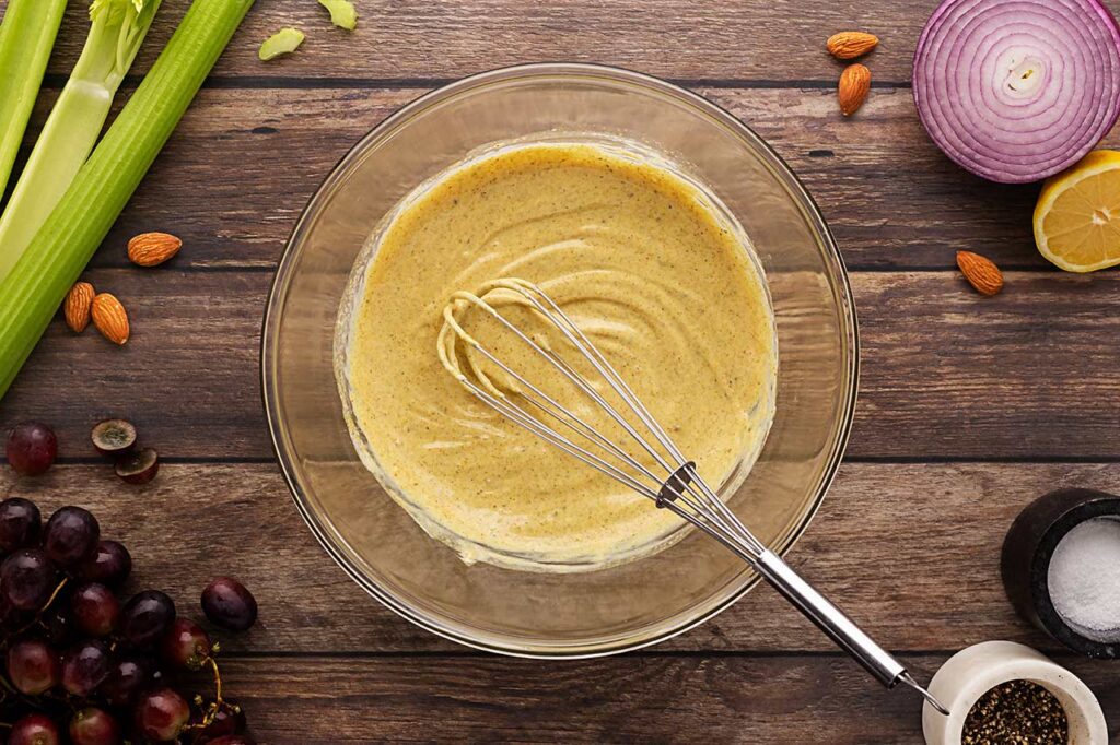Mixed dressing for curry chicken salad in a mixing bowl with a whisk. Overhead focus.