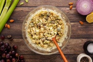 Curried chicken salad mixed with dressing in a mixing bowl with a wood spoon. Overhead focus.