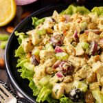 Front, partial view of curried chicken salad on a black plate with salad greens.