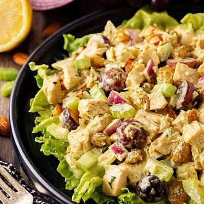 Front, partial view of curried chicken salad on a black plate with salad greens.