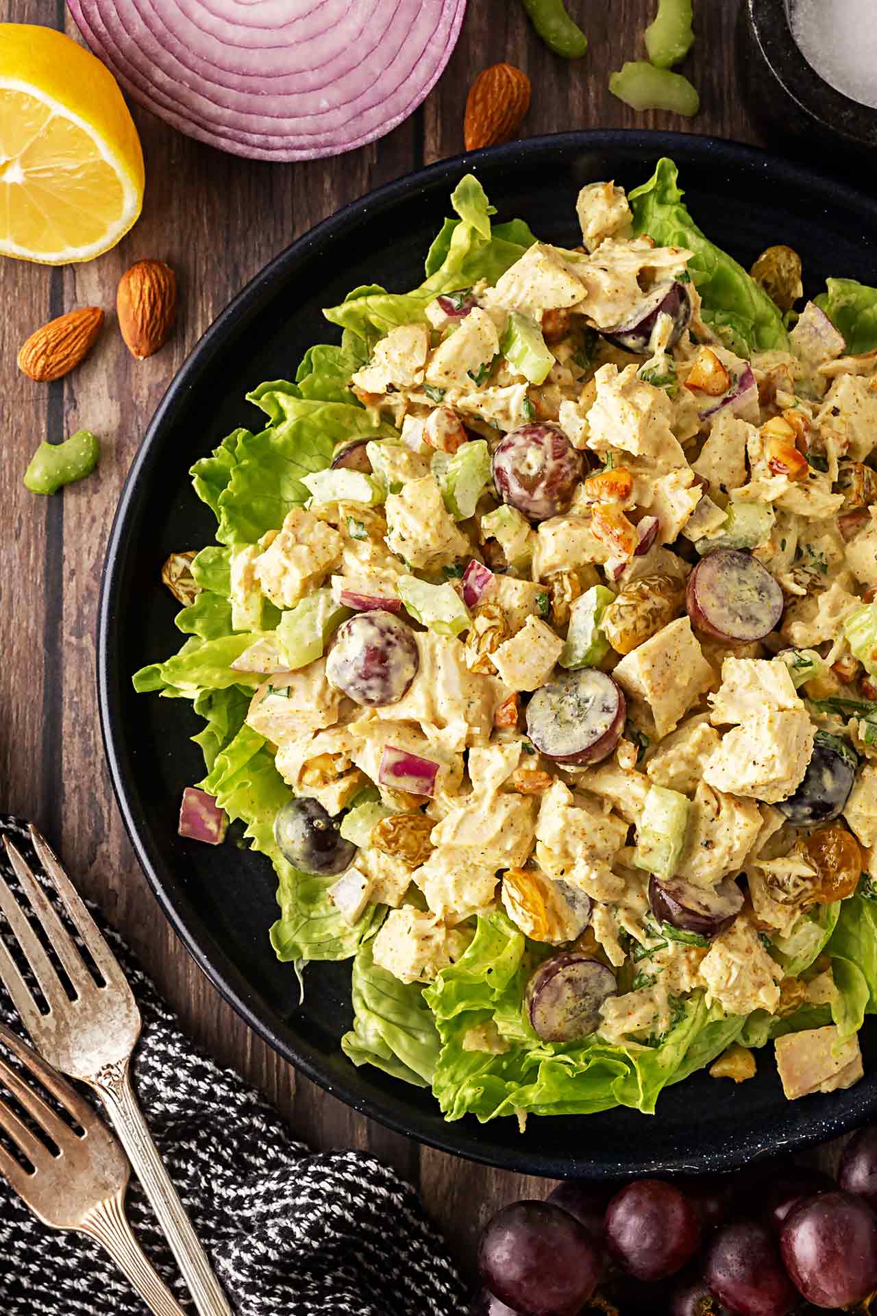 Overhead focus. Black plate holds a bed of lettuce greens and curried chicken salad served over the top.
