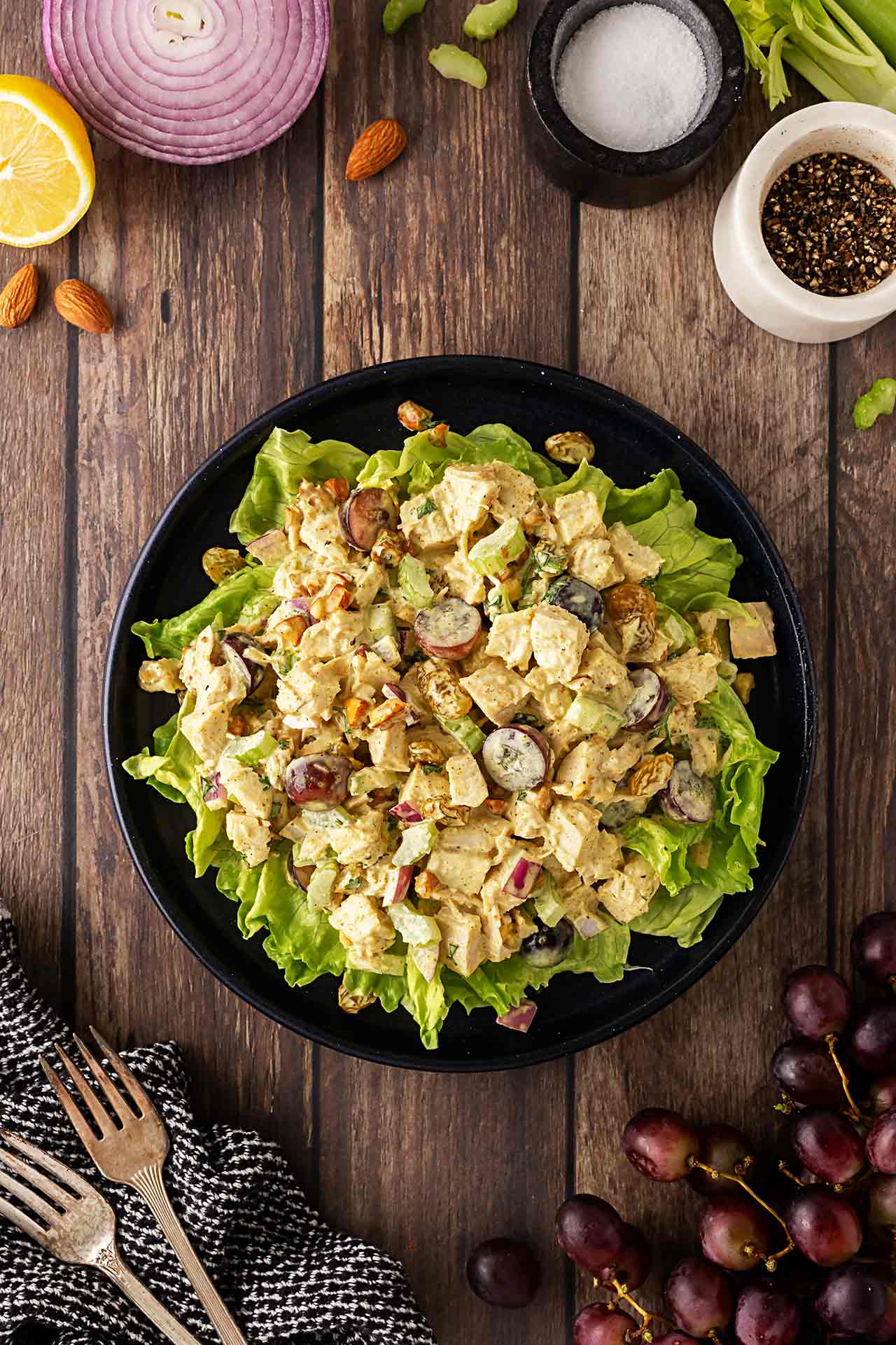 Overhead focus. Curried chicken salad served over salad greens on a black plate on a wooden surface.