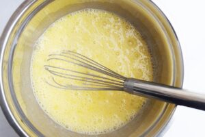 Mixed wet ingredients in a metal bowl with a whisk resting in the bowl.