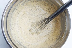 Whisked High-Protein Bread batter in a metal mixing bowl with a whisk resting in the bowl.