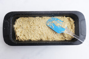 Batter in a loaf pan with a rubber spatula resting on top after smoothing out the batter.