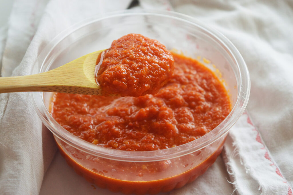 Side view of a wood spoon lifting Homemade Sriracha Sauce out of a tub.