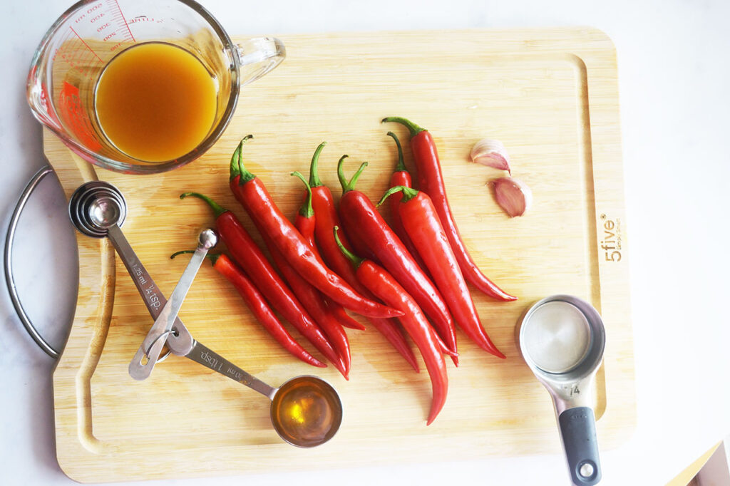 Homemade Sriracha Sauce recipe ingredients gathered on a wood cutting board.
