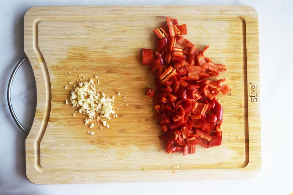 Cutting board with chopped red chili peppers and minced garlic.