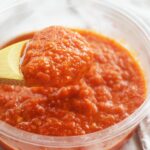 Front view of a wood spoon holding a spoonful of Homemade Sriracha Sauce.