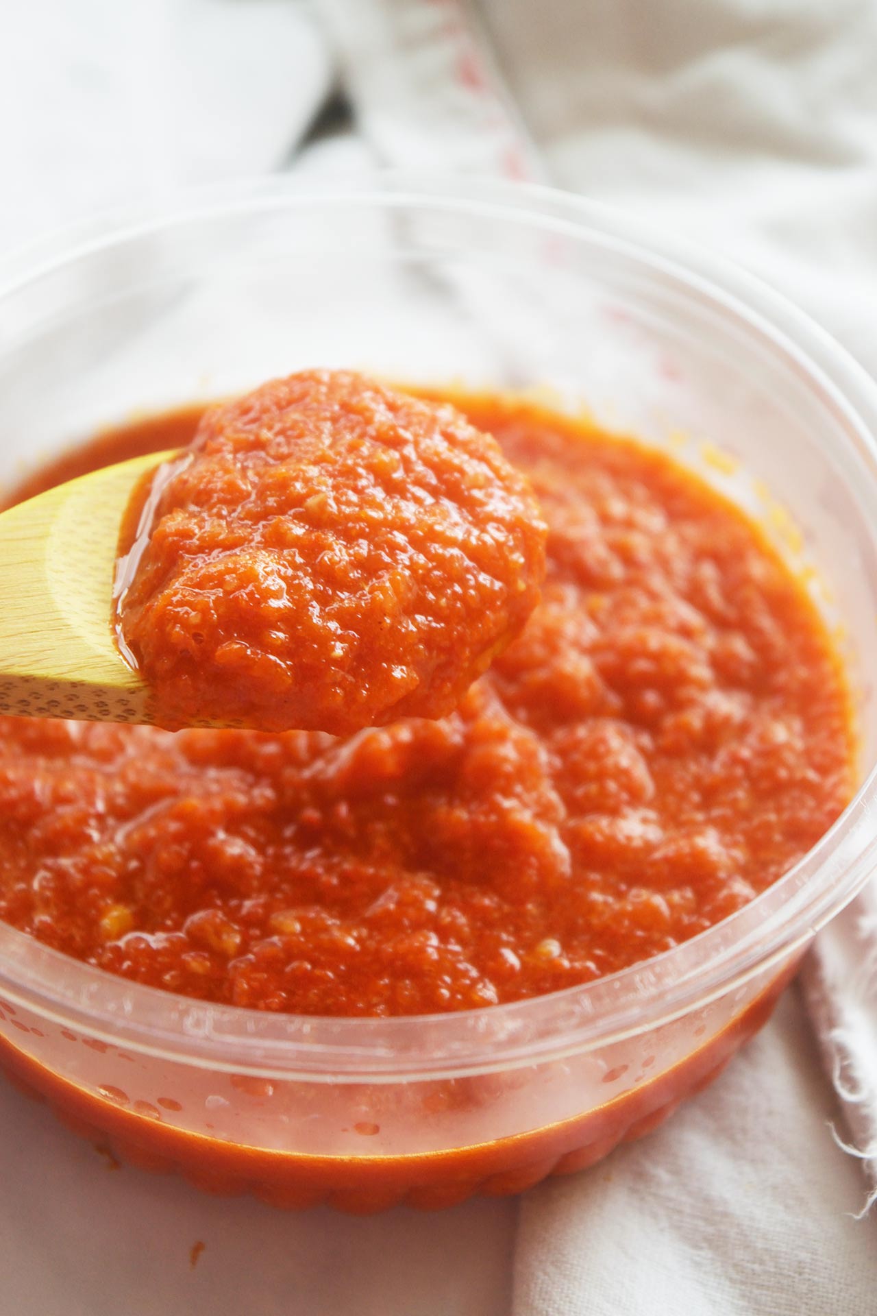 Front view of a wood spoon holding a spoonful of Homemade Sriracha Sauce.